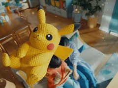 A close-up of a Pikachu plush toy with a playful expression, floating in a cozy room background.