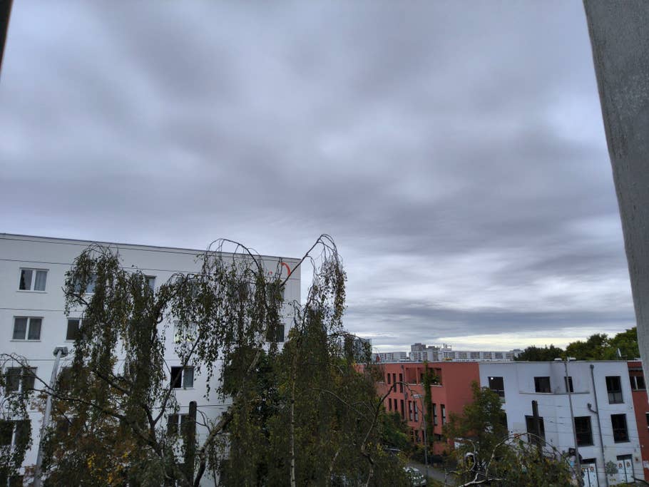 Cloudy sky over buildings with trees in the foreground.