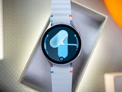 A Samsung Galaxy Watch 7 displayed in a box with a blue and white strap showing a digital watch face.