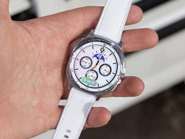 A person holding a Samsung Galaxy Watch 8 Classic with a white strap, displaying various watch faces.