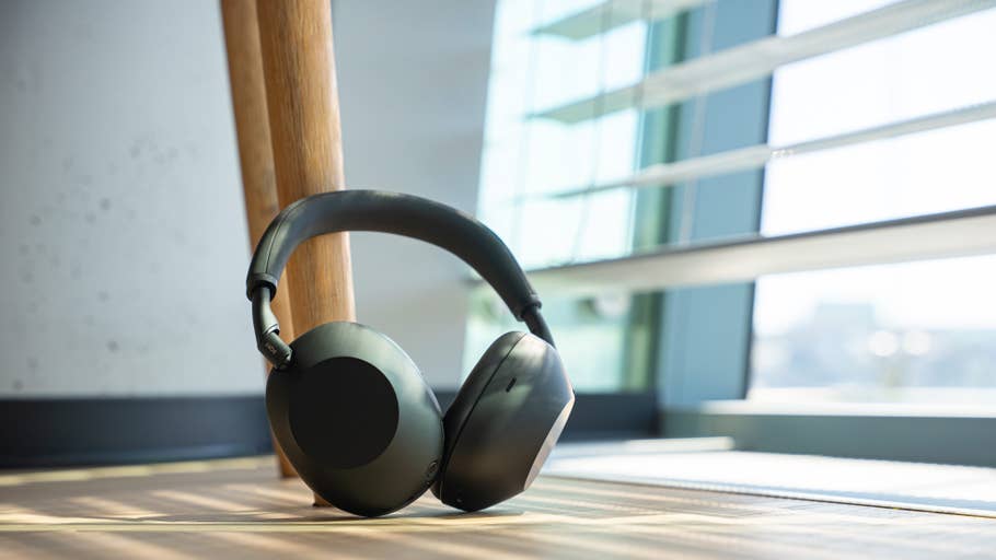 A pair of Sony WH-1000XM6 headphones lies on a wooden floor next to a window.