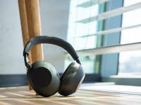 A pair of Sony WH-1000XM6 headphones resting on a wooden floor near a window.