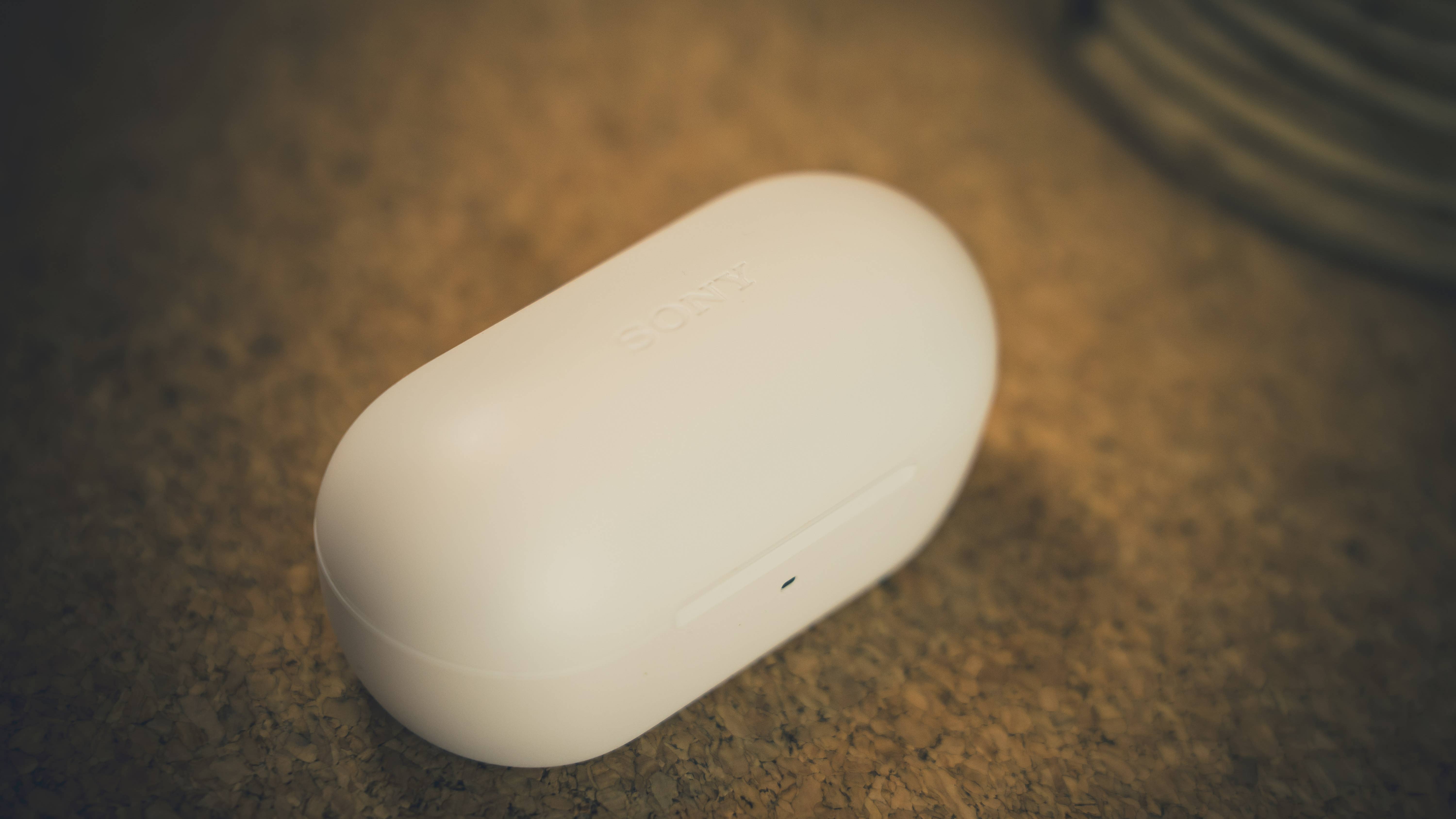 A white Sony earbuds case on a cork surface.
