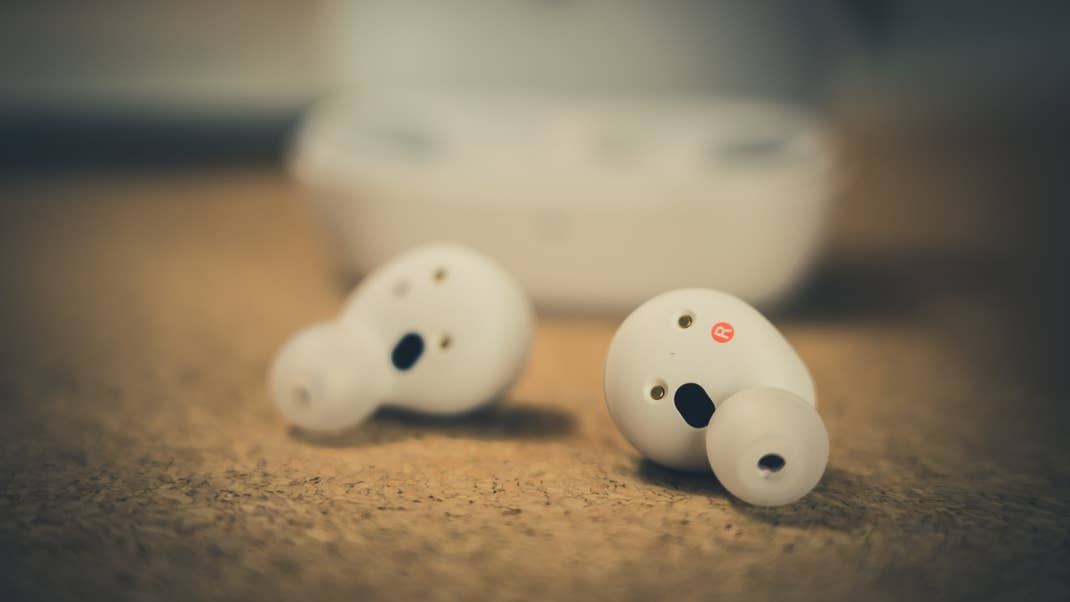 Close-up of Sony wireless earbuds on a cork surface with their charging case in the background. Close-up of Sony wireless earbuds on a cork surface with their charging case in the background.