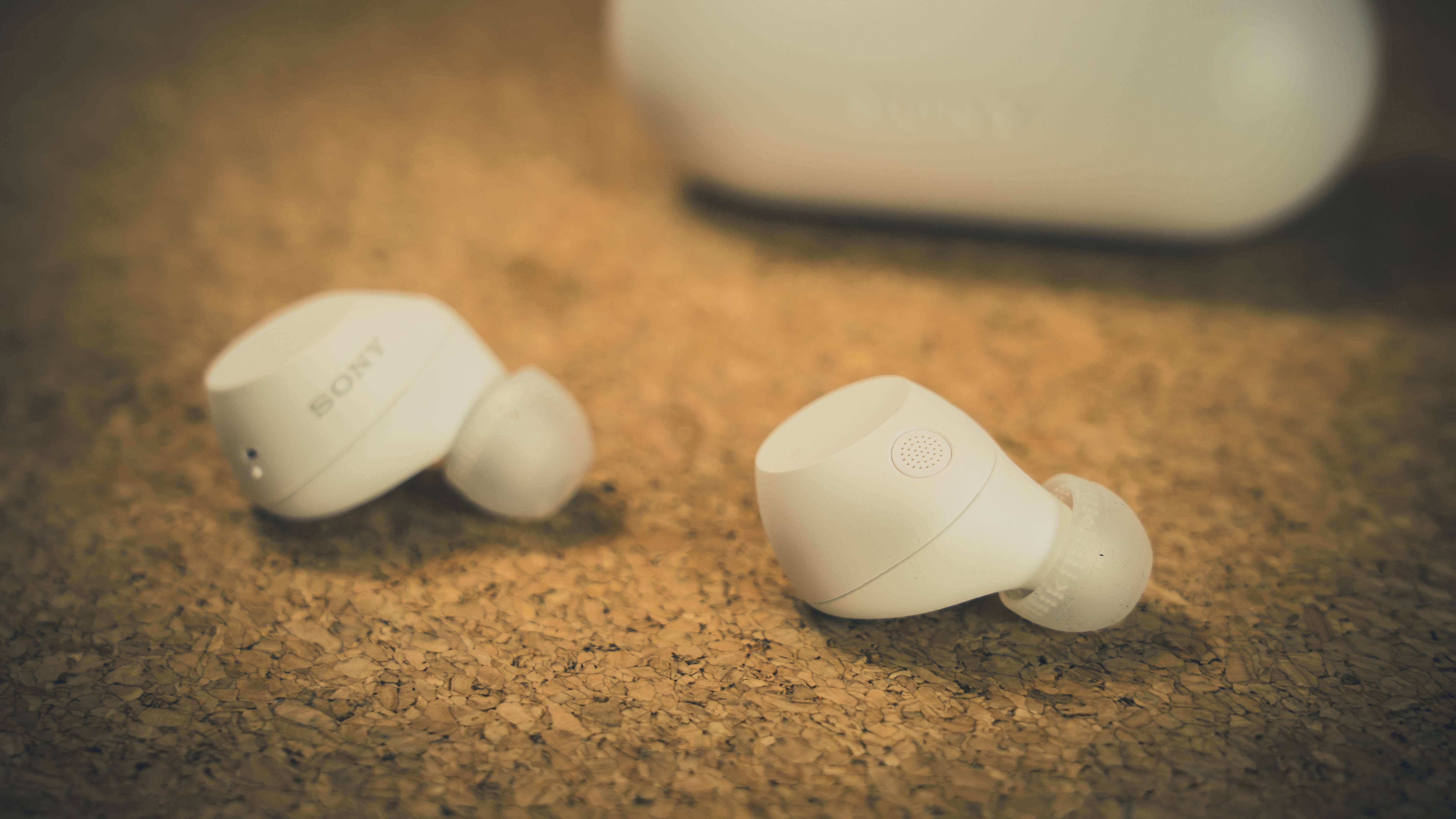 White Sony earbuds on a cork surface with a charging case in the background.