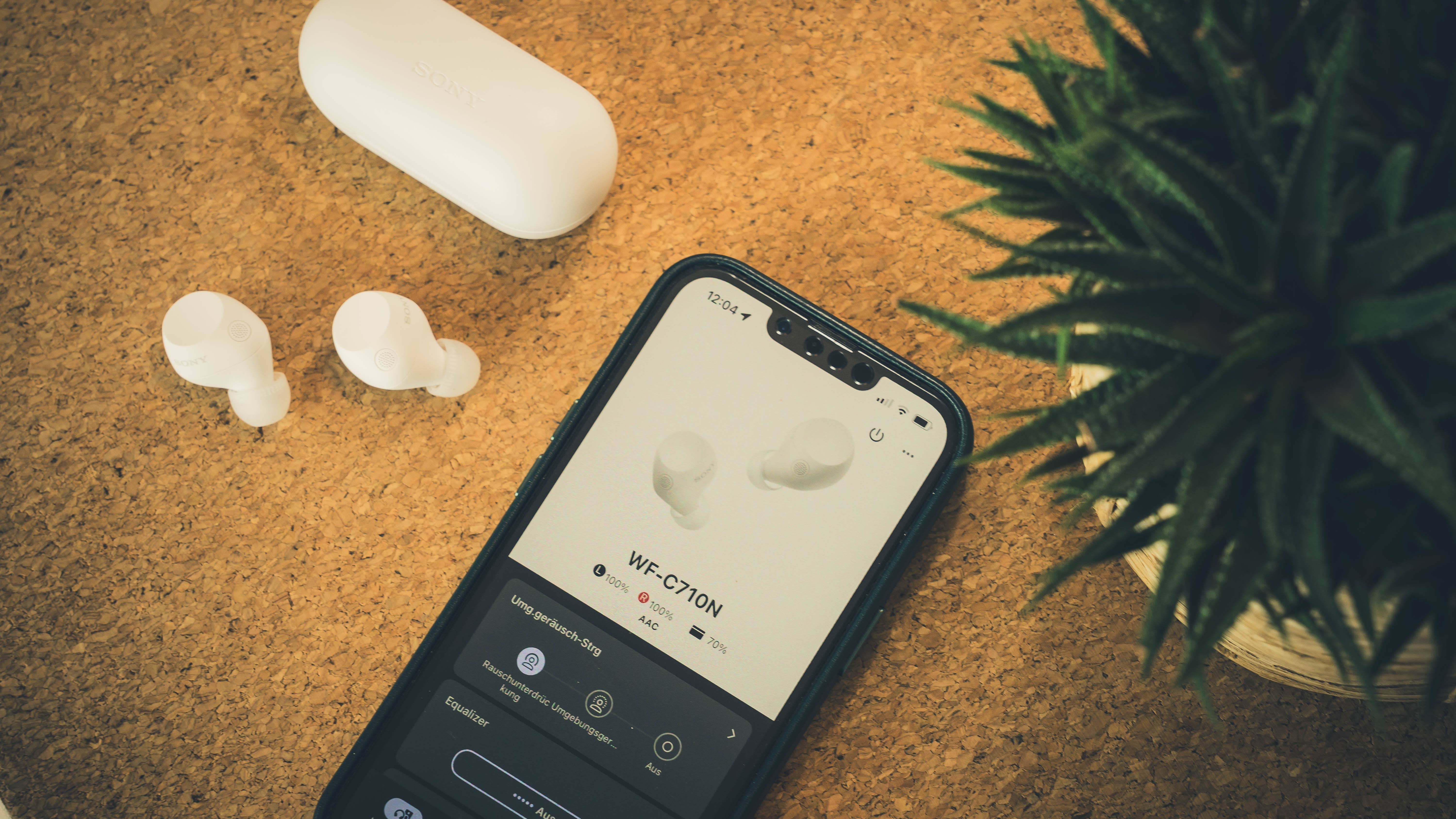 White Sony wireless earbuds with charging case and phone displaying the WF-C710N interface.