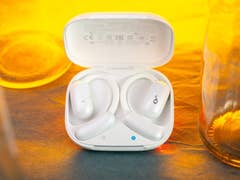 White Soundcore Aerofit 2 earbuds in an open charging case with a warm background.