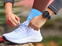 Amazfit Active 3 Premium on the wrist of a woman lacing up her running shoe.