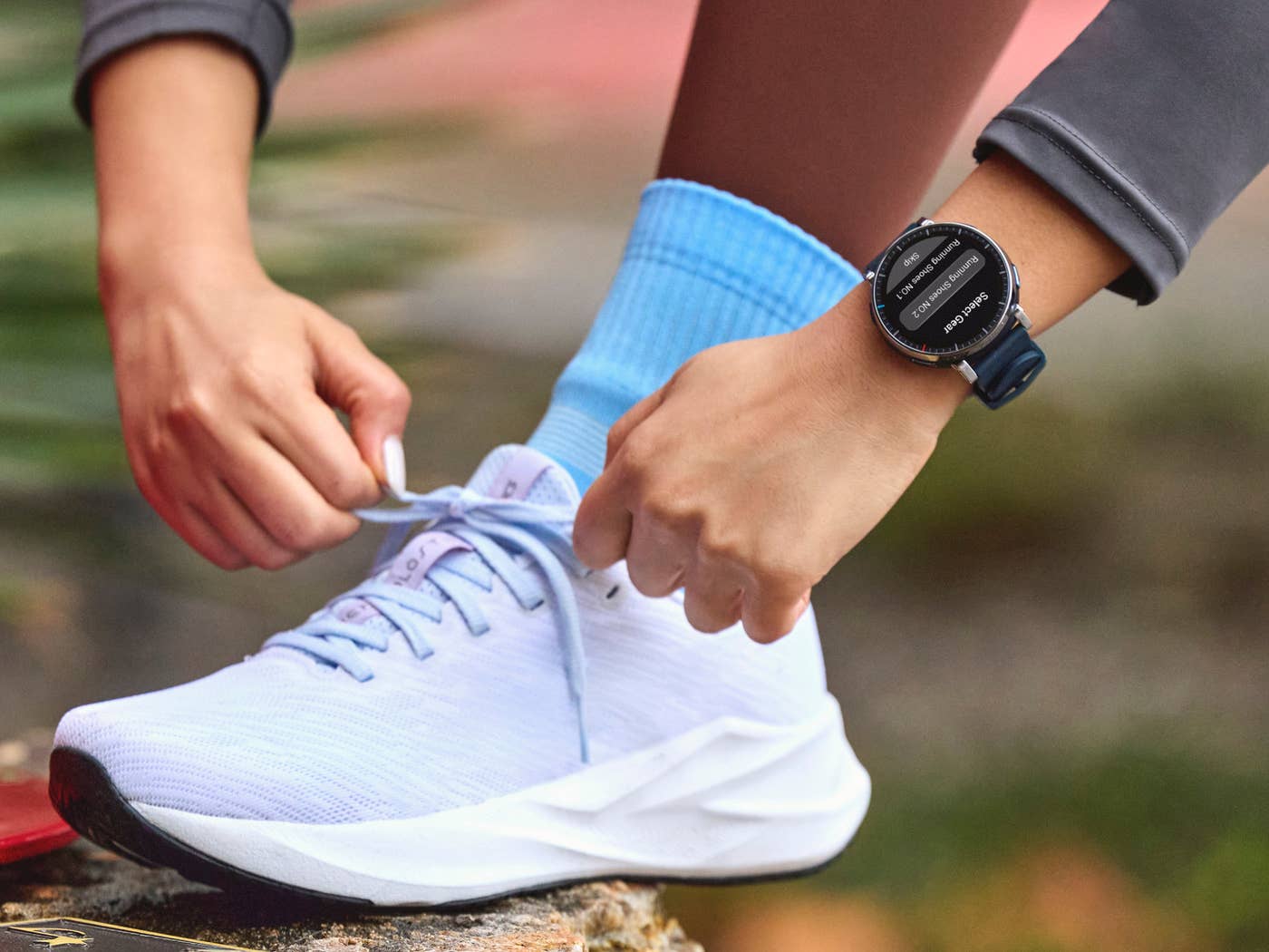 Amazfit Active 3 Premium on the wrist of a woman lacing up her running shoe.