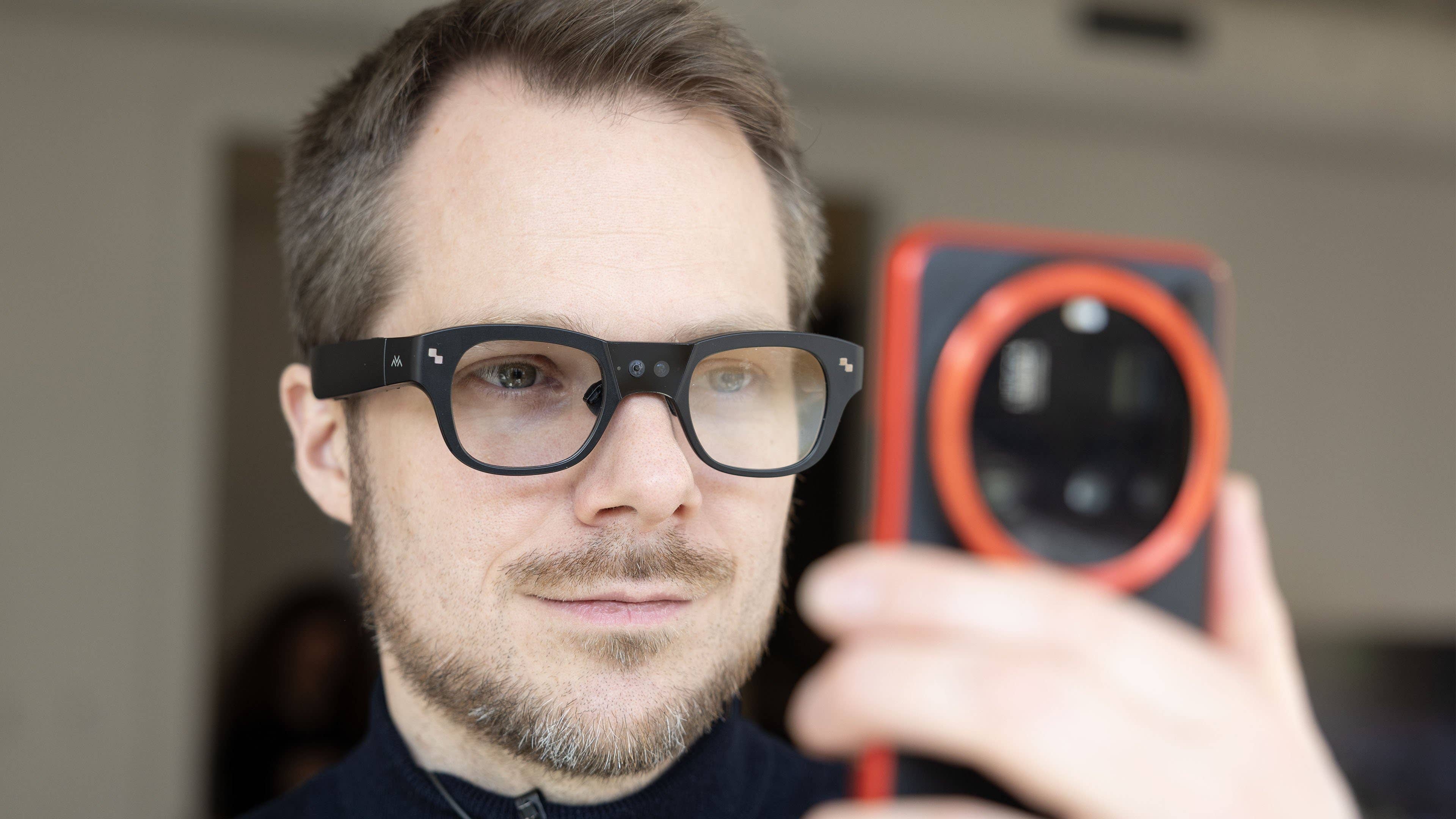 A man wearing smart glasses is looking at a smartphone camera.