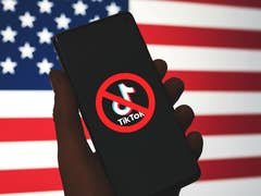 A hand holding a smartphone displaying a 'No TikTok' symbol against a US flag background.