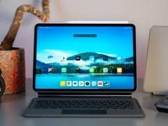 A Xiaomi Pad 7 on a desk with a keyboard, a camera, and a potted plant in the background.