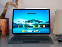 A Xiaomi Pad 7 on a desk with a keyboard, a camera, and a potted plant in the background.